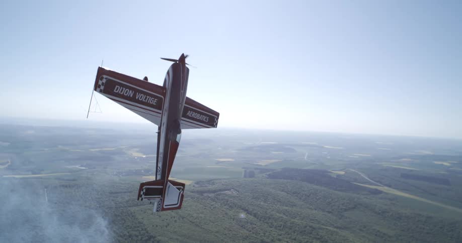 Against a backdrop of brilliant blue sky and a delicate wisp of cloud an aerobatic plane hangs vertically above a sprawling green landscape