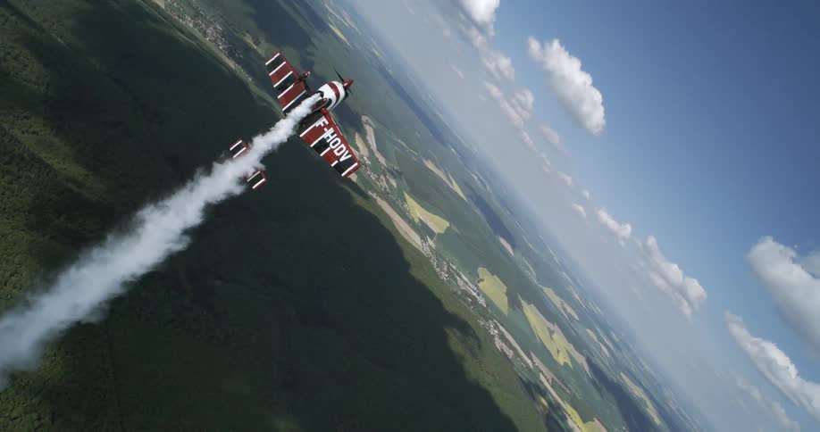 A stunt plane releases smoke as it soars above a vast forest landscape