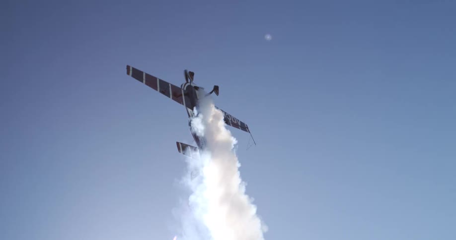 A small propeller plane performs a vertical aerial stunt trailing white smoke against a clear blue sky
