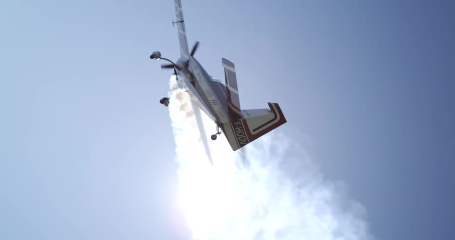 An airplane performs an aerobatic maneuver with a smoke trail curling behind it against a clear blue sky