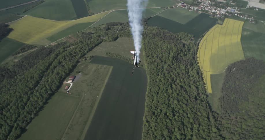 A stunt plane climbs vertically over farmland leaving a smoke trail