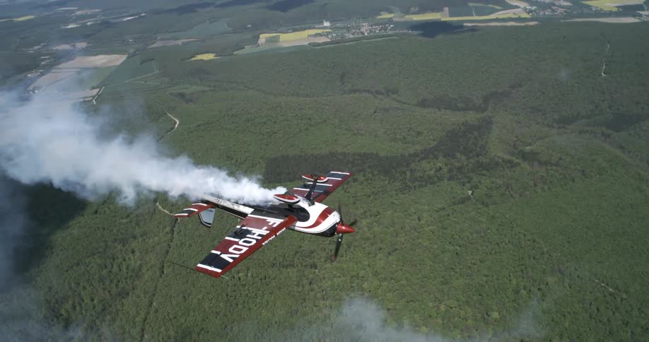 Small plane releasing smoke flying over a forest area
