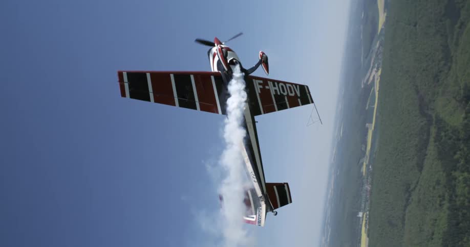An acrobatic plane ascends vertically trailing smoke against a clear blue sky