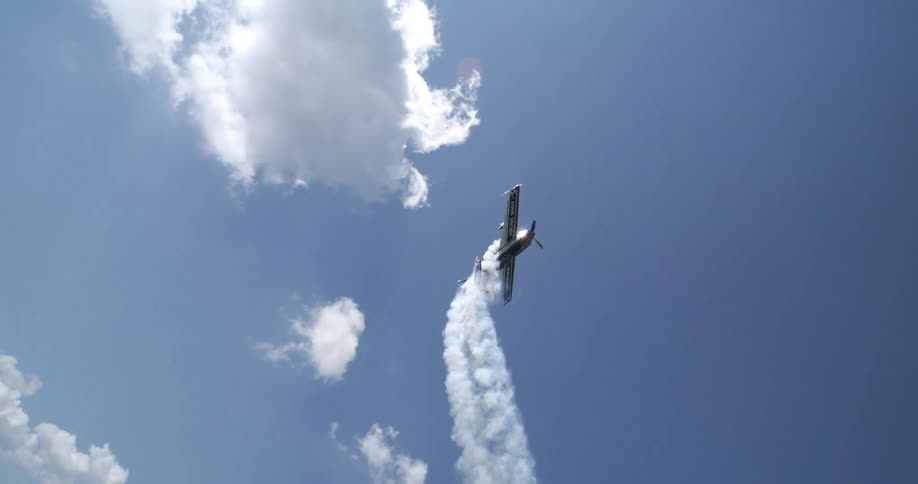 A small stunt plane ascends vertically into a clear blue sky trailing thick white smoke