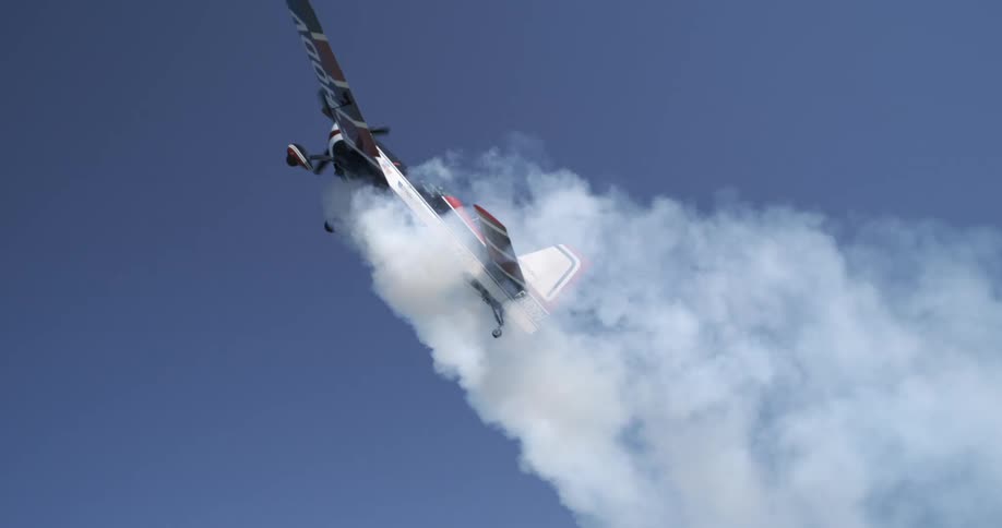 Single engine plane flying in a blue sky and releasing smoke