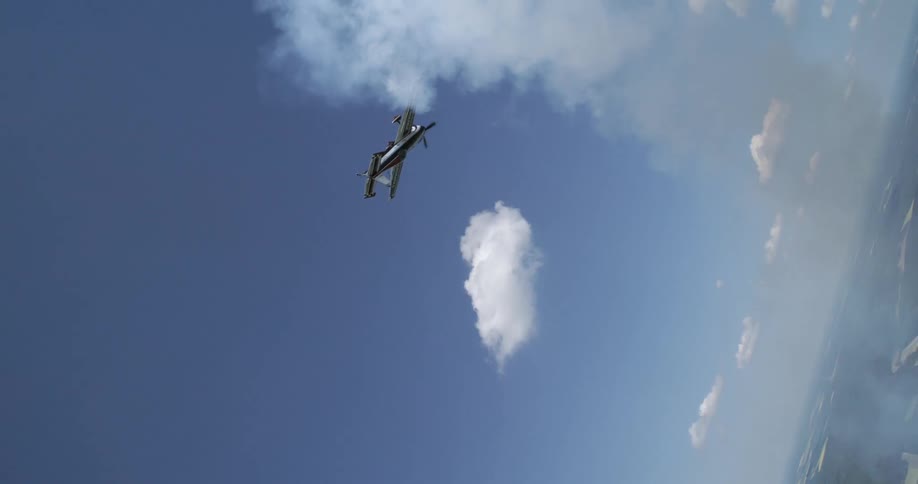 A small airplane performs an aerobatic loop trailing white smoke against a backdrop of blue sky and scattered clouds