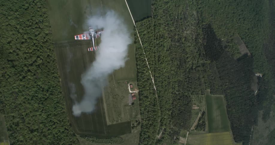 Single engine plane releasing smoke and flying over a forest area