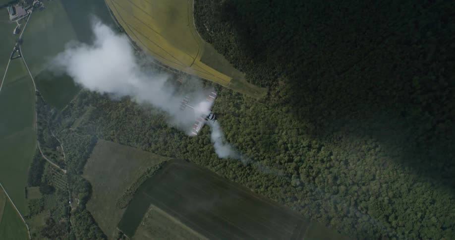 An aircraft crashes in a forested area trailing thick smoke as seen from an aerial view