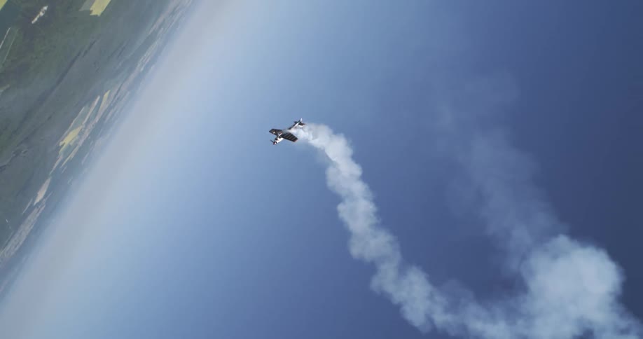 Stunt plane spirals upward with smoke trail against tilted earth