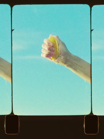An adult hand squeezes juice from an orange on a sunny day