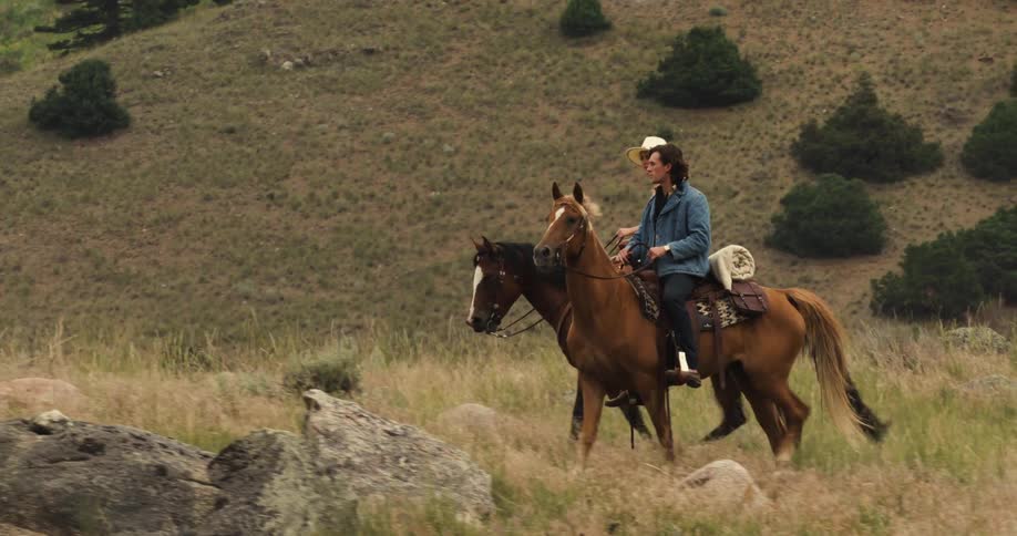 Couple horseback riding across grassy hillside in a rural area