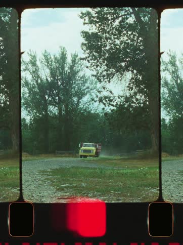 A yellow truck is driving on a gravel road surrounded by tall trees