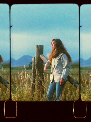 Woman in jacket and jeans leaning against a fence in a field