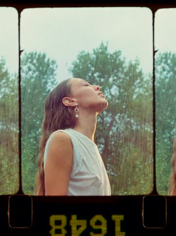 Young woman looks to the sky while standing outdoors under the rain during daytime