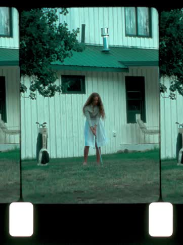 Girl in a white dress stands in front of a white house seemingly preparing to swing a golf club