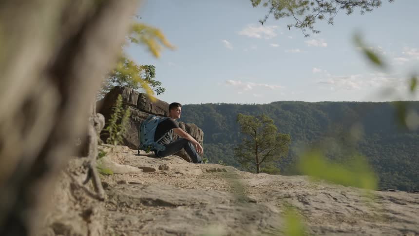 Man wearing blue backpack sits on a cliff