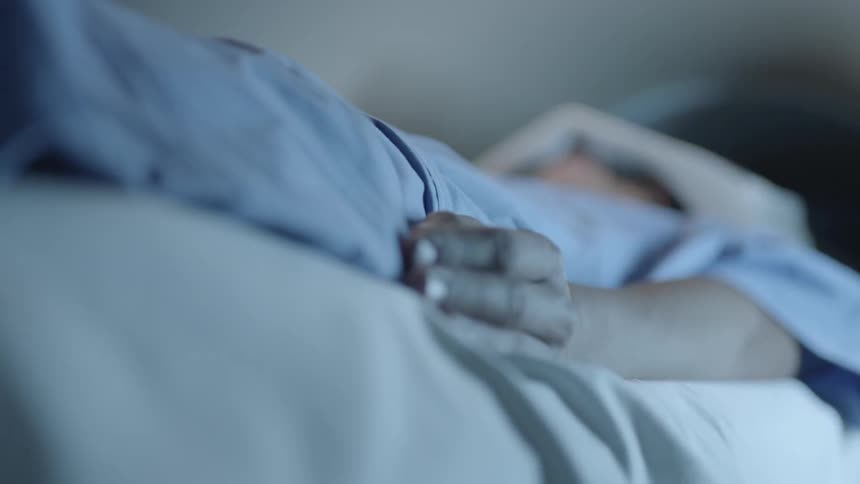 Person lays on a bed wearing a hospital gown