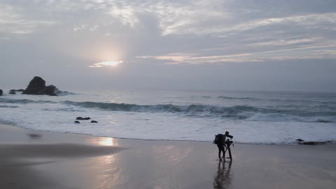A photographer is standing on a beach with a tripod at dusk