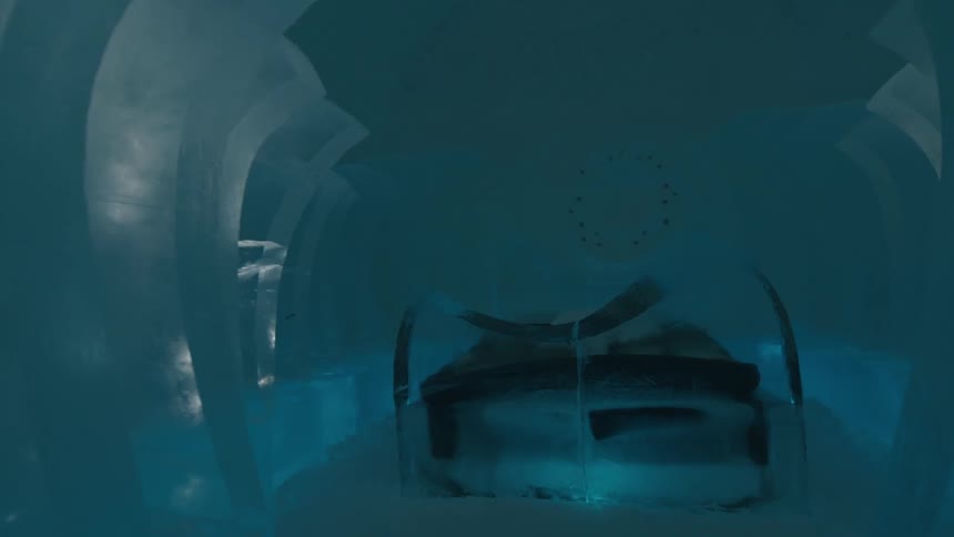 Walking through a corridor of sculpted ice in an ice hotel reveals a bedroom with a bed framed by an icy headboard