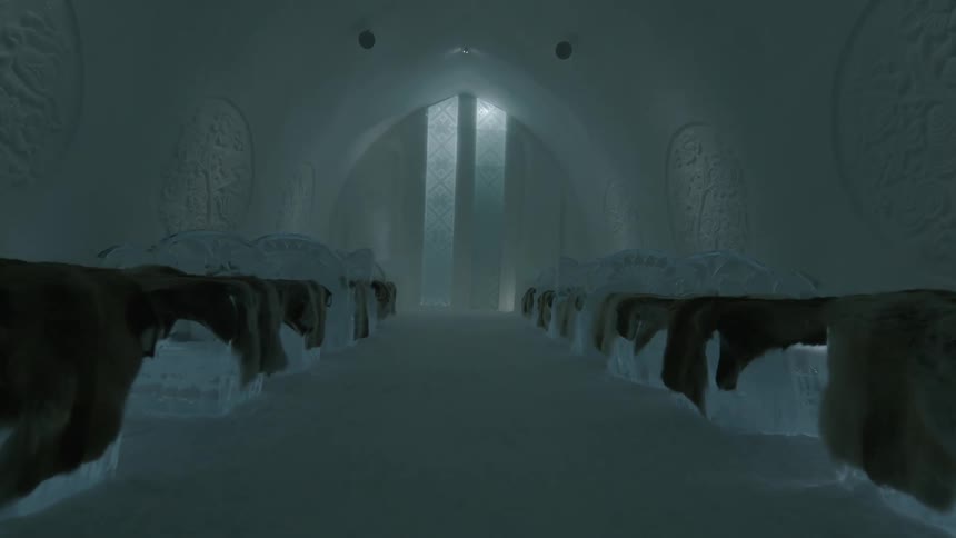 An indoor view shows a room made of ice with beds lined up on both sides leading towards an illuminated archway at the far end