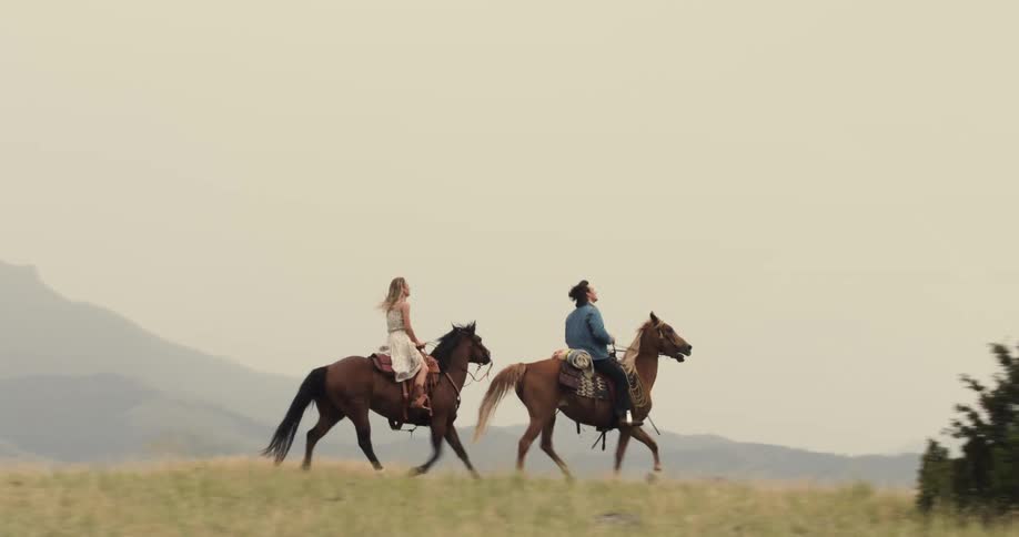 Man and woman riding horses in a mountainous setting