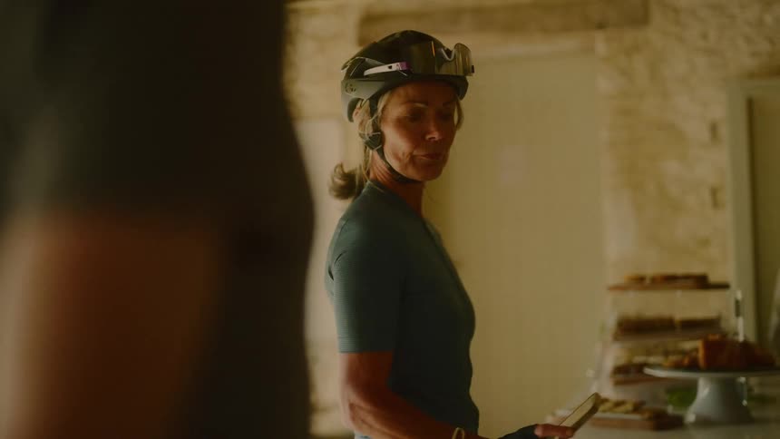 A woman in a bike helmet and fingerless gloves checks her smartphone in a rustic room