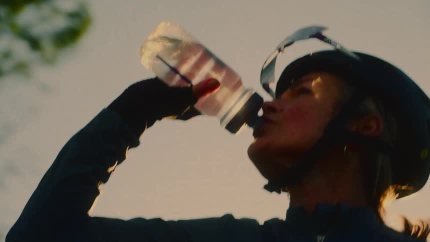 A cyclist in a helmet drinks from a water bottle outdoors