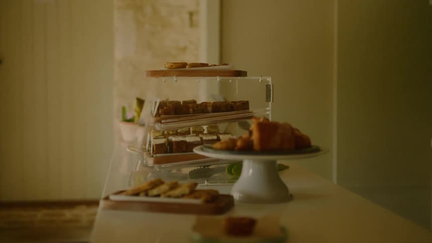 A softlit indoor buffet setup featuring assorted pastries neatly arranged on trays and a cake stand