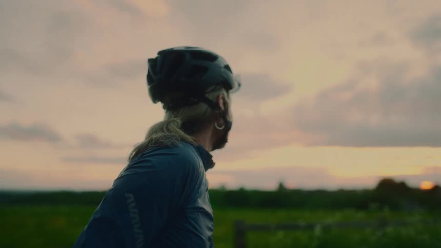 Female cyclist pauses in the rural countryside to look around with a smile on an overcast day