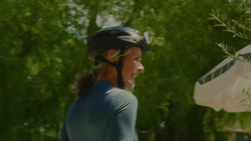 A woman is standing with her back turned wearing a helmet and walking forward next to a white sombrero and some trees