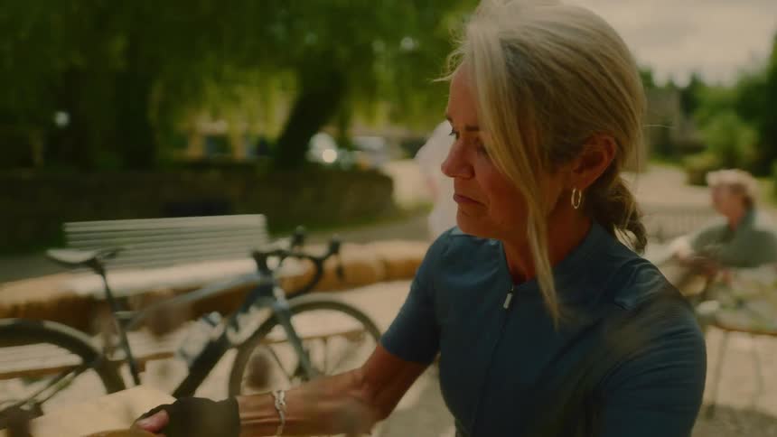Female cyclist is sitting outdoors drinking from a cup