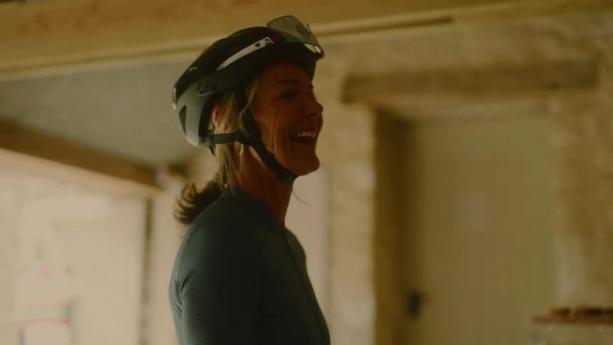 A smiling woman wearing a helmet chats indoors in warm lighting