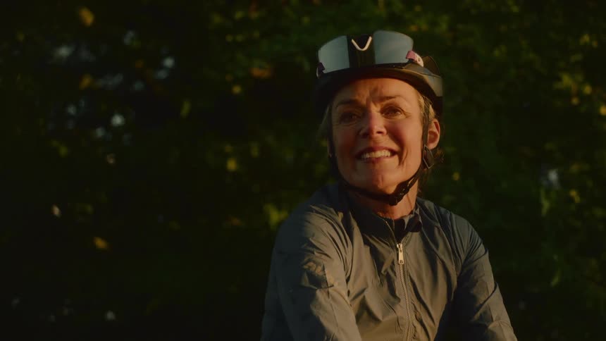 A smiling cyclist pauses during a ride in warm evening light surrounded by trees
