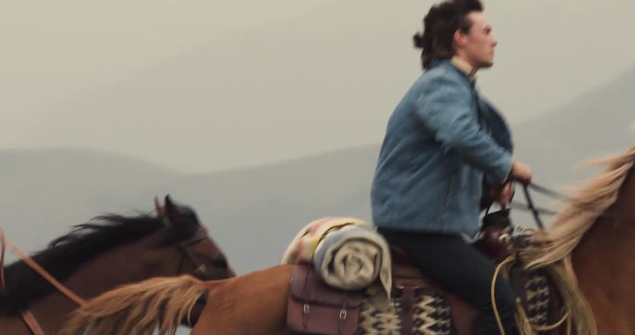 A man and woman ride horses through the mountains