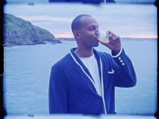 A man near the seashore drinking juice from a glass cup
