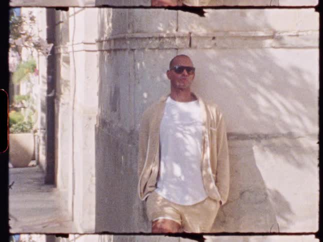 Bald man with sunglasses leaning against a wall on an urban sidewalk