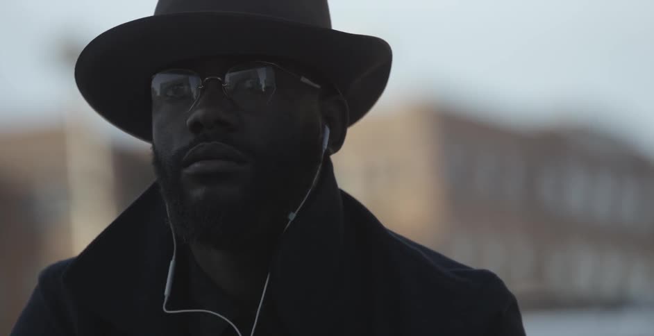 Man wearing a hat standing outside with headphones in his ears