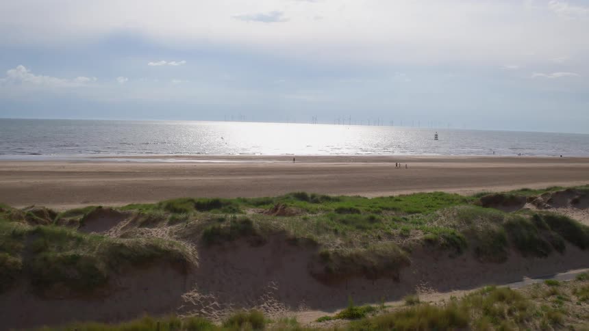 People walk on a sandy beach beyond the grass dunes