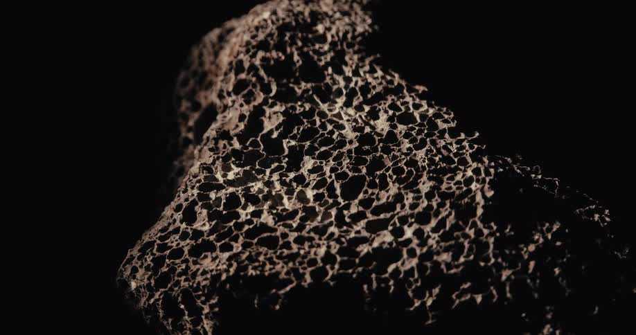 Rock with small holes and debris against a dark background
