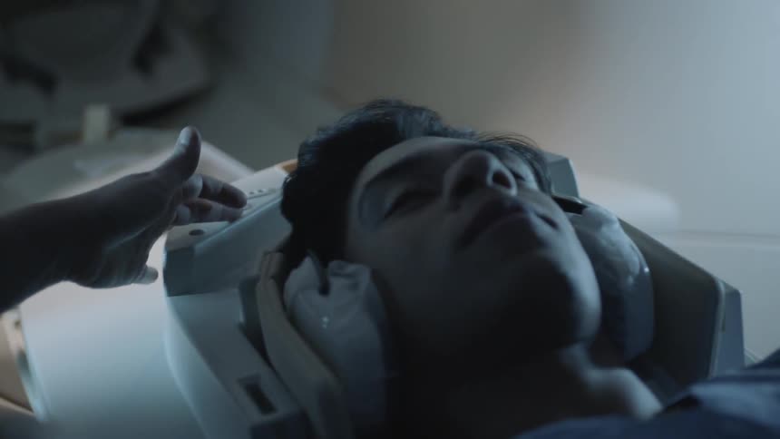 A technician puts earphones and equipment on a patient lying on a table