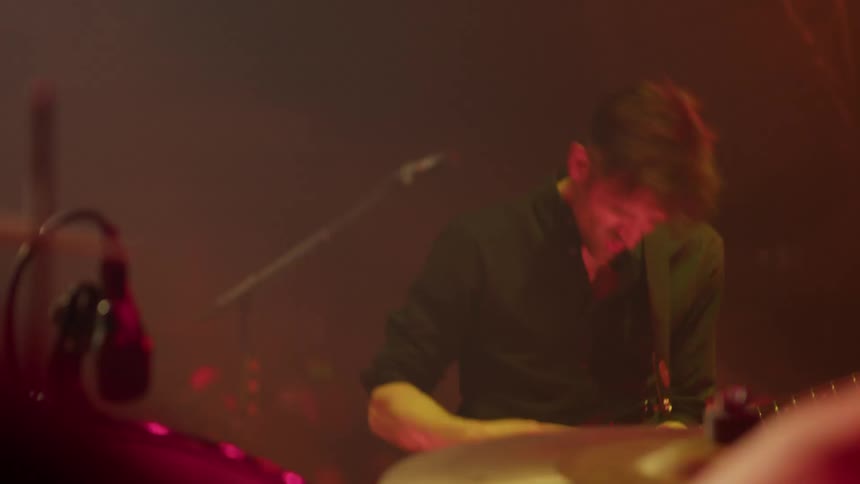 Musicians perform energetically on stage under warm dramatic lighting during a live concert