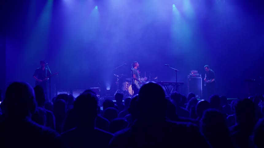 A rock band performing on stage for a large crowd in a club