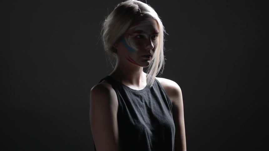 A woman with paint on her face rotates forward in a dark room