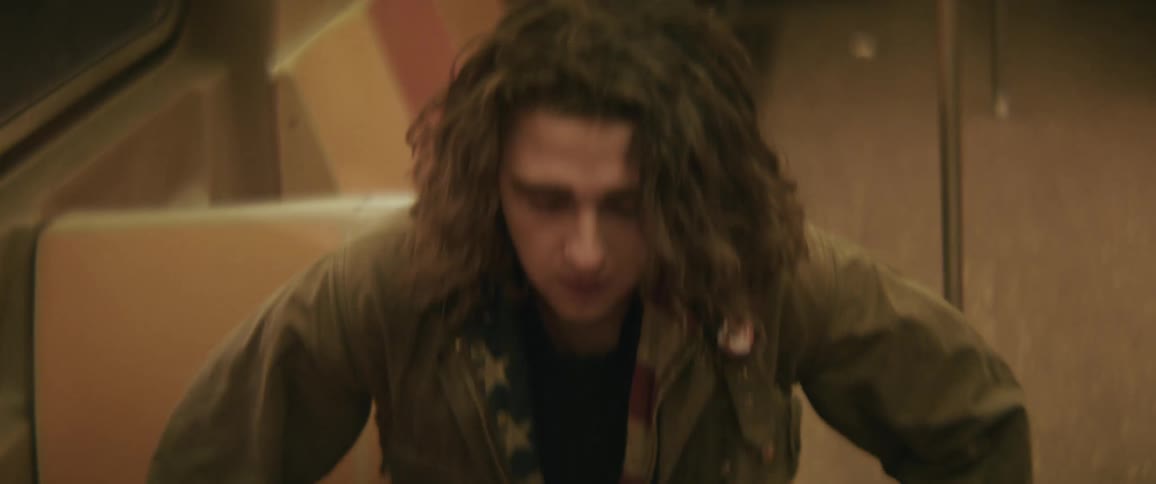 A young man with long hair wearing a jacket enters a train and takes a seat his expression somber and reflective