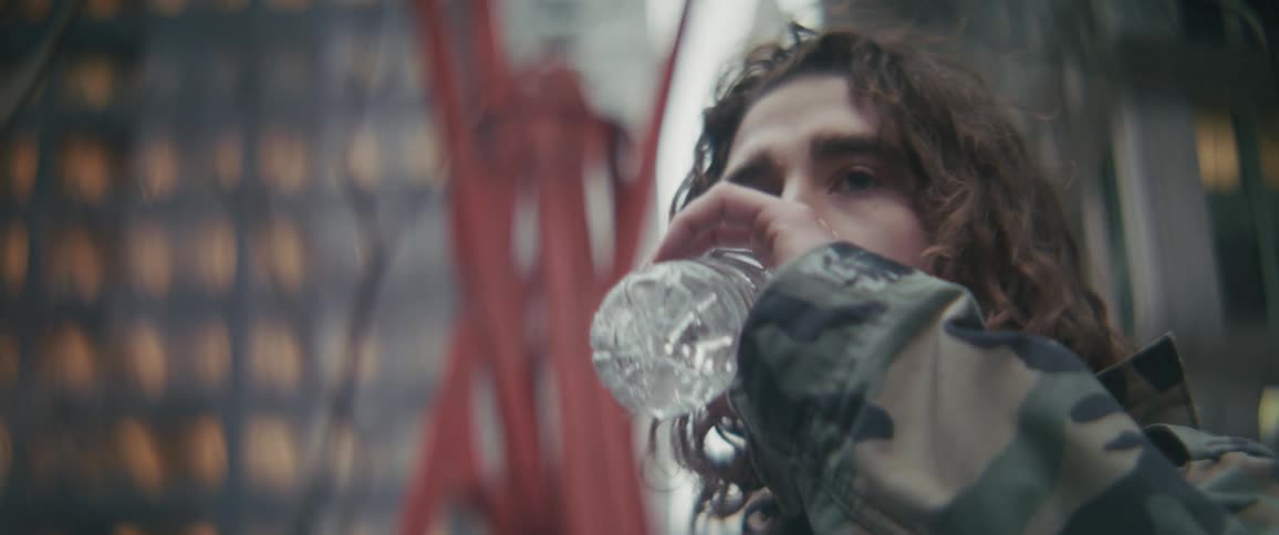 Curly haired man drinking water outdoors