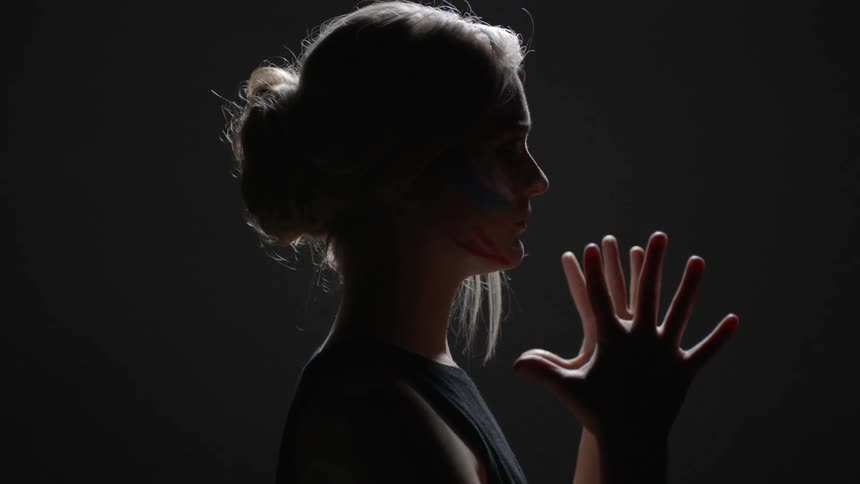 A woman wearing face paint lowers her hands