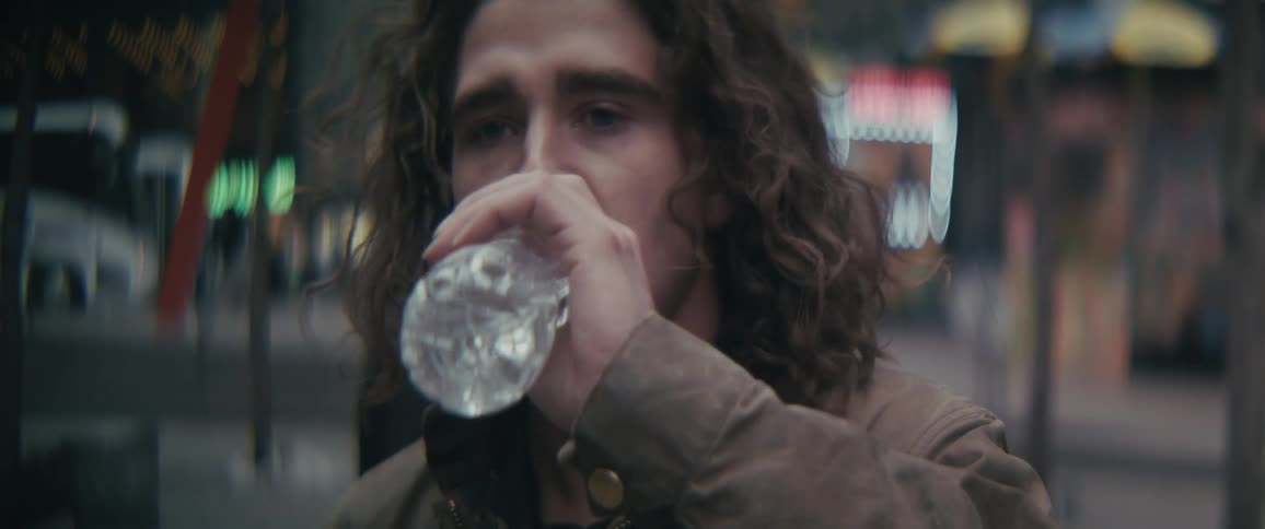 Worried man approaches the camera and takes a drink of water while many people walk around behind him