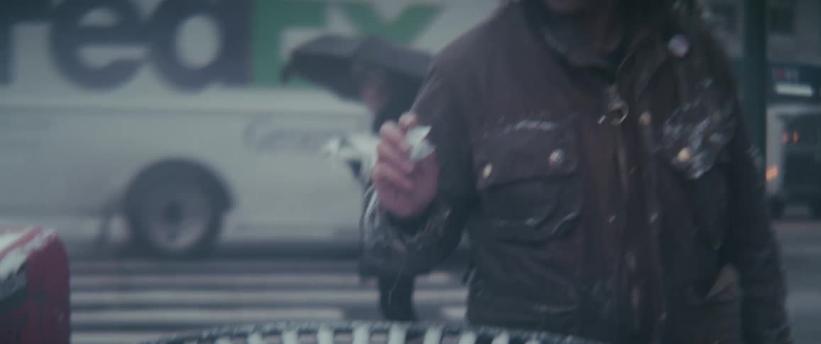 A man walks towards a bin in the city and throws something in it while people stands and cars move around at dawn
