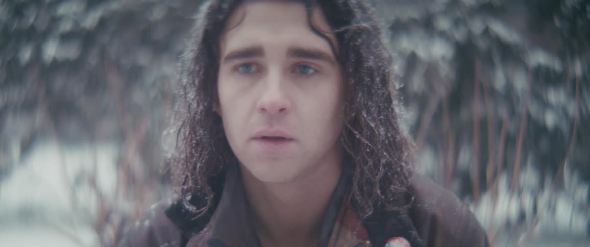 The face of a curly haired man who is looking forward and it is snowing in his hair