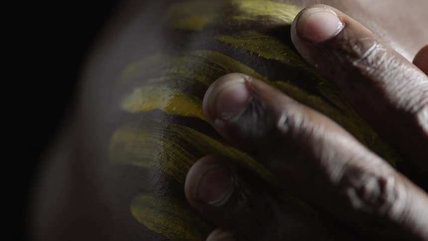 Hand smearing yellow paint down a shoulder